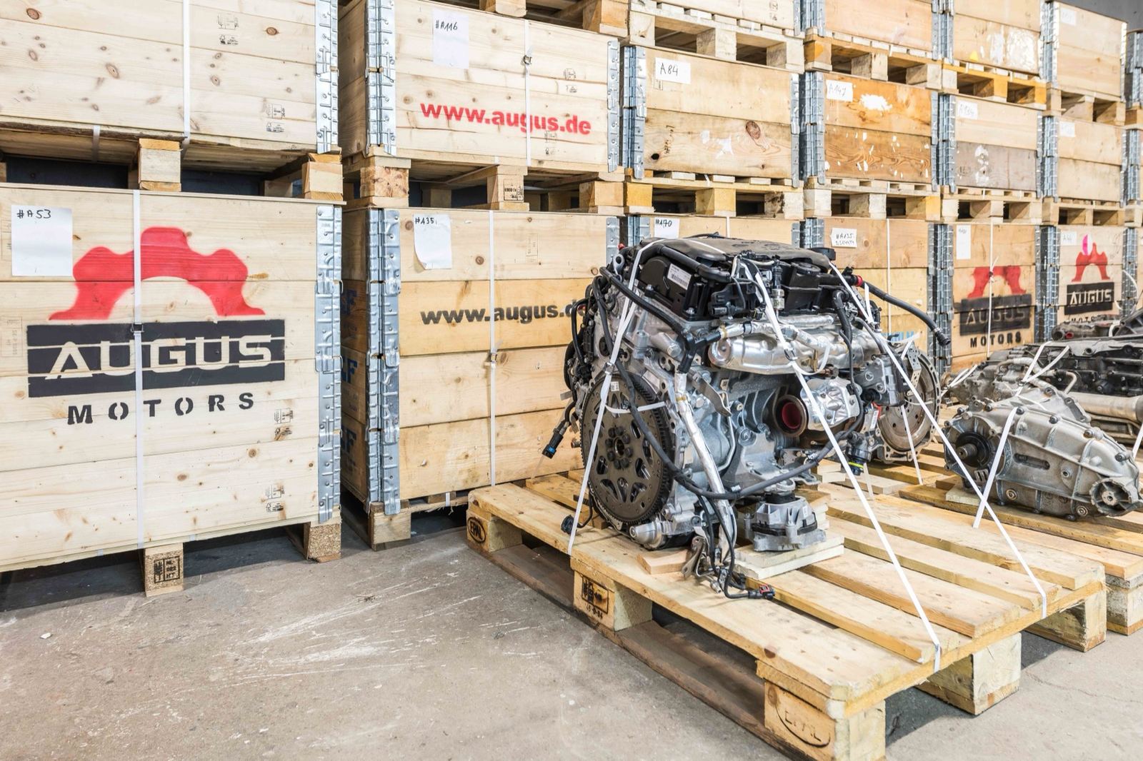 Austauschmotor auf einer Palette vor gestapelten Augus-Motors-Transportkisten im Lager