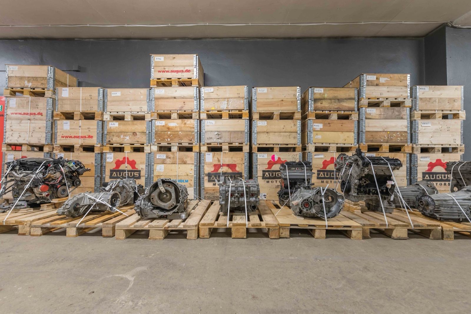 Motoren und Getriebe auf Paletten vor gestapelten Transportkisten im Lager von Augus Motors